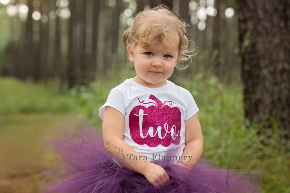 Two year old girl portrait in the woods with purple tutu