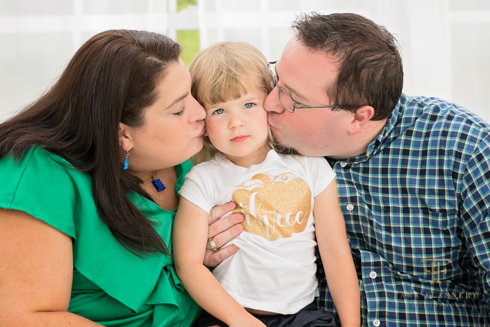 mom and dad kissing little girl family photos
