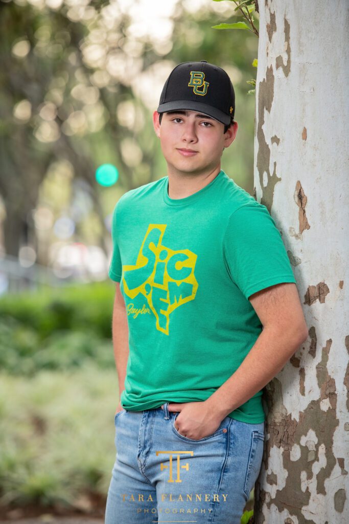 High school senior boy poses for a photo in his Baylor college shirt and hat.