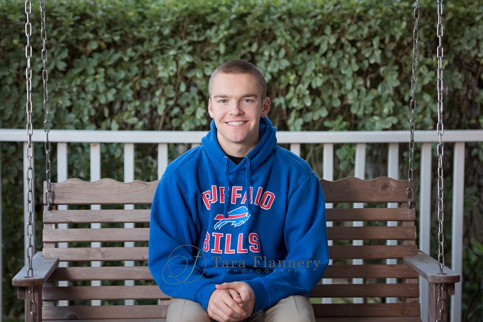 high school senior with sweatshirt sitting on porch swing