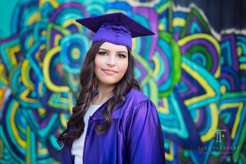 high school senior in cap and gown with graffiti wall