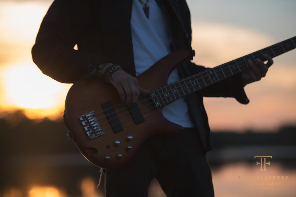 high school senior poses with bass guitar at sunset