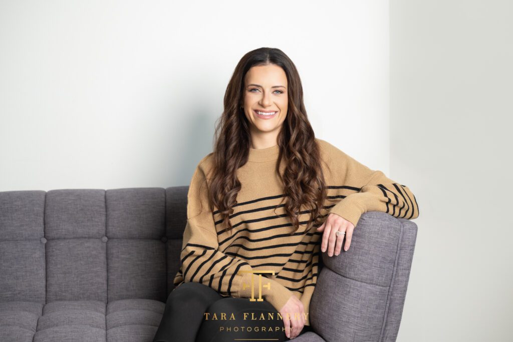 Branding photo of woman sitting on a grey couch.