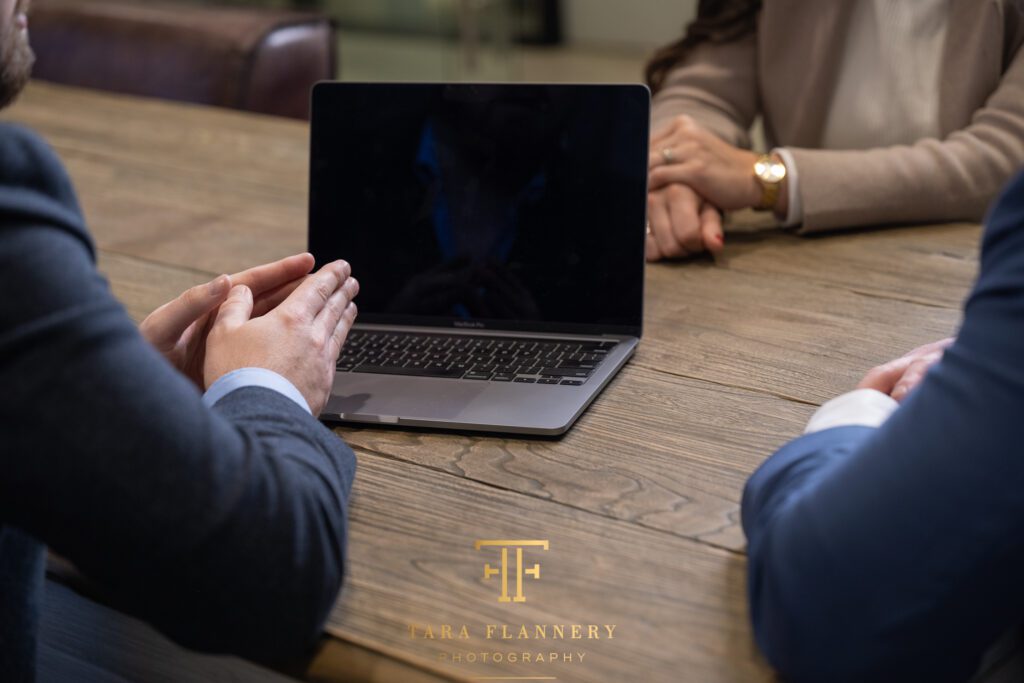 Branding photo of computer and people's hands around a conference table.
