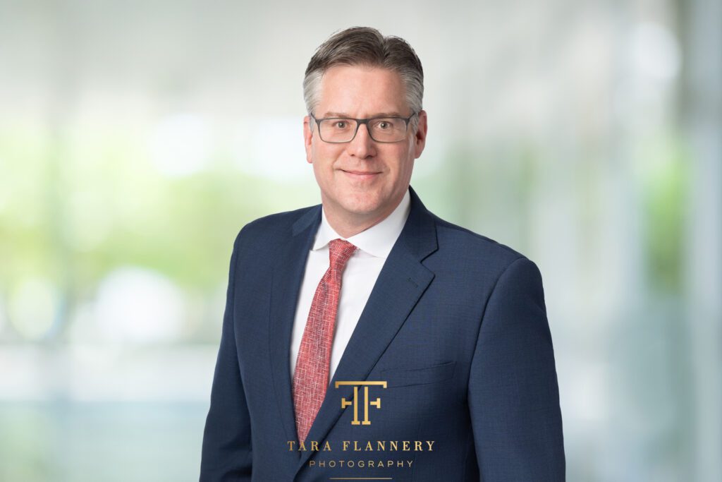 Man in blue suit jacket and tie poses for a professional headshot in Houston.