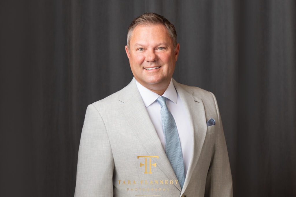 Man in light colored suit smiles for a CEO professional headshot.