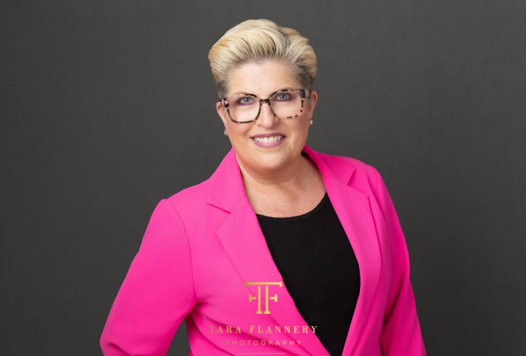 Business headshot for a woman in bright pink suit jacket.