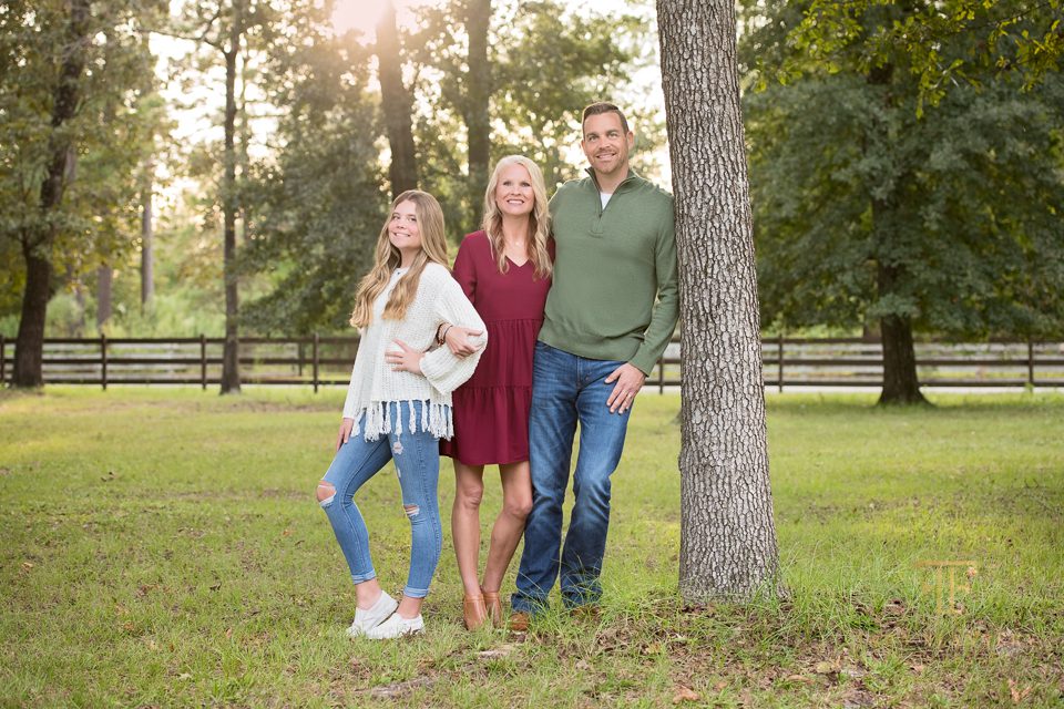 Family of three smiles at the camera during their outdoor family portrait session in The Woodlands TX.