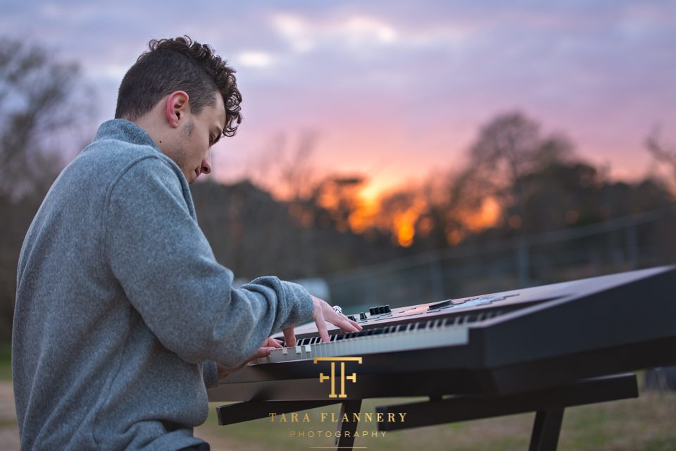 Boy plays the keyboard in front of the setting sun for his senior photography session in The Woodlands TX.